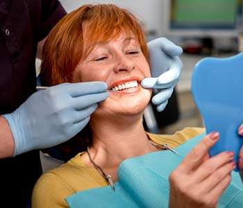 Smiling senior woman with new dental sealent sitting in the dental office and looking at the mirror