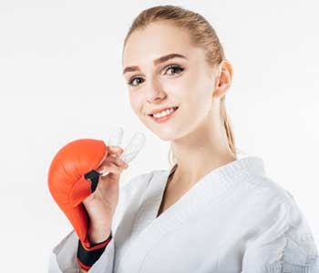 smiling female karate fighter holding mouthguard isolated on white